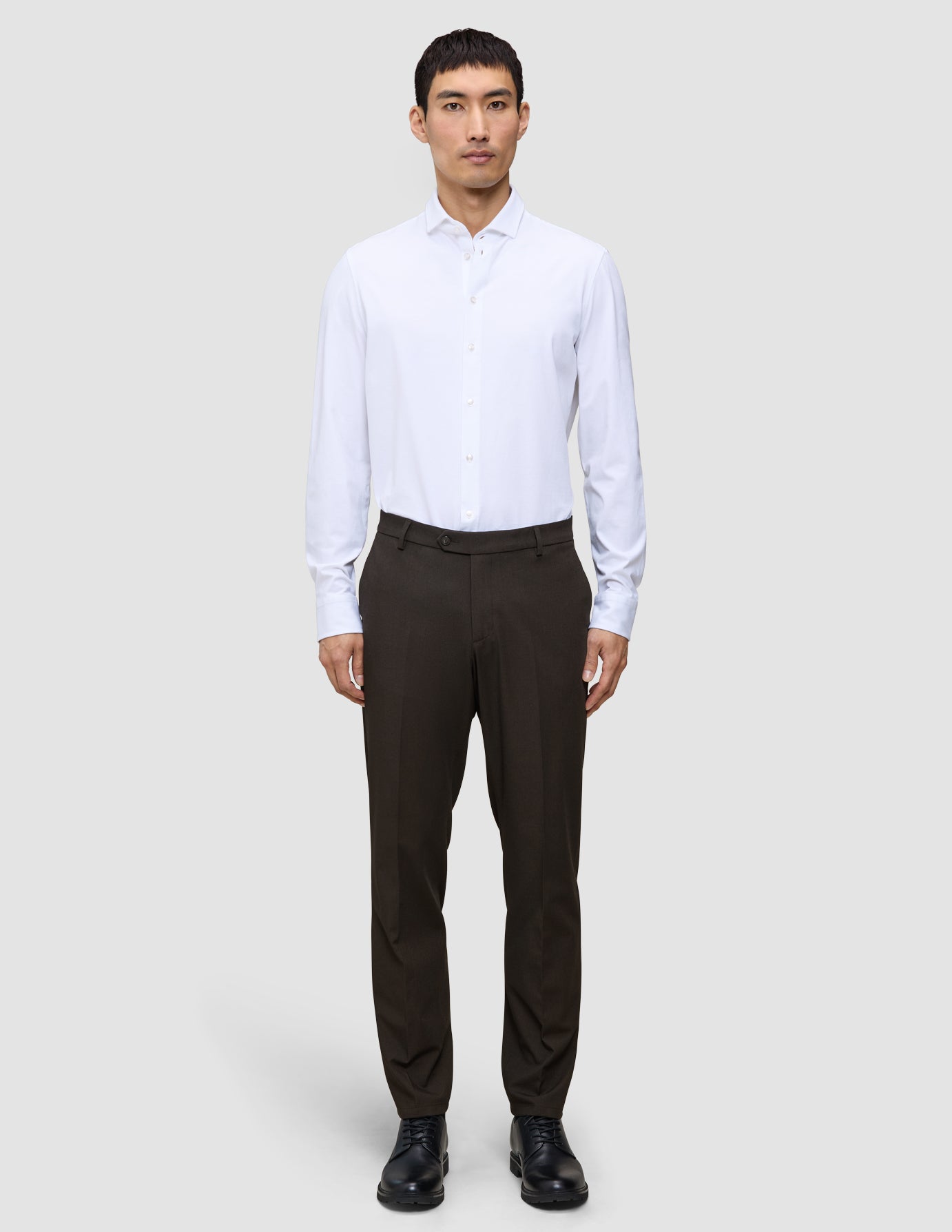 En mand iført en hvid skjorte med knapper, Motion Suit-bukser i Regular-pasform i farven Cognac og sorte sko.